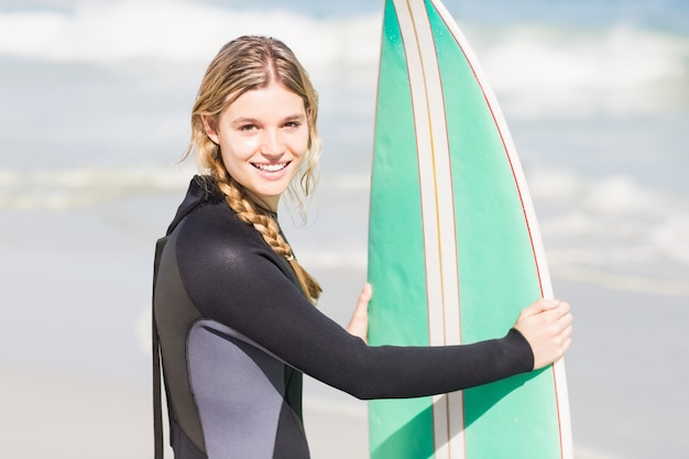 Retrato de mujer en traje de neopreno con una tabla de surf en la playa