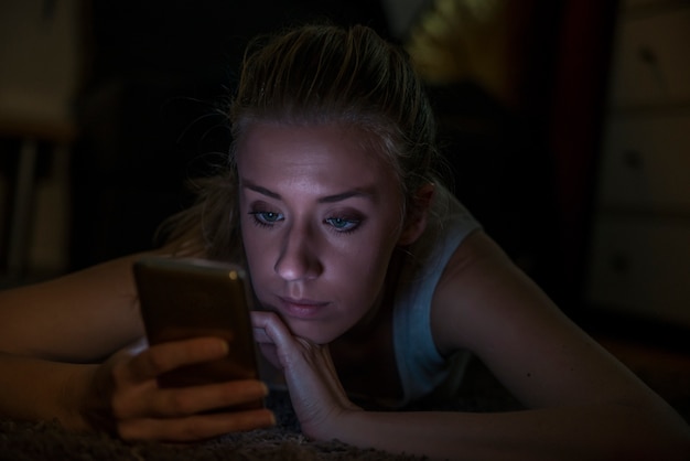 Retrato de una mujer trastornada que lee un mensaje de texto en su teléfono en la noche en el país