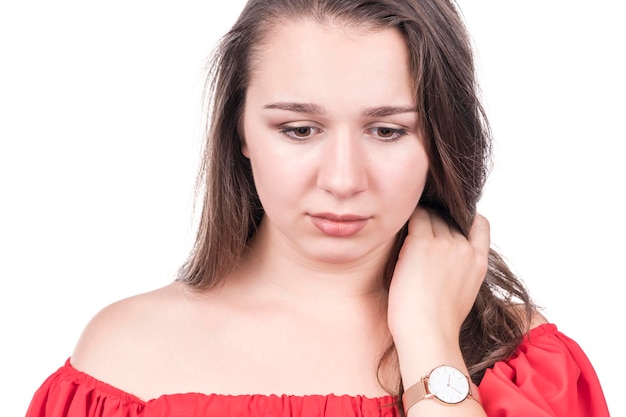 Retrato de mujer triste en blusa roja con la mano cerca del cuello mirando hacia abajo, aislado sobre fondo blanco.