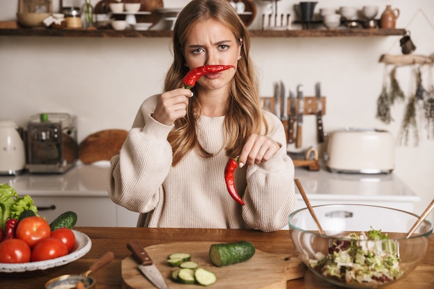 Retrato de mujer triste linda vistiendo ropa casual haciendo muecas mientras se cocina la cena en la acogedora cocina