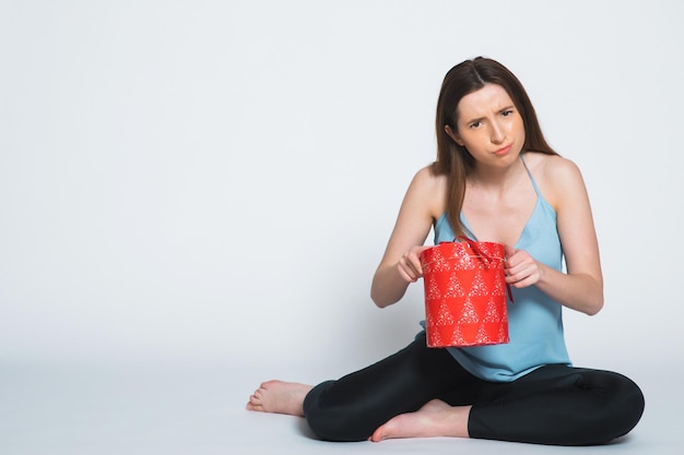 Retrato de una mujer triste de pie con una caja de regalo abierta aislada en un blanco