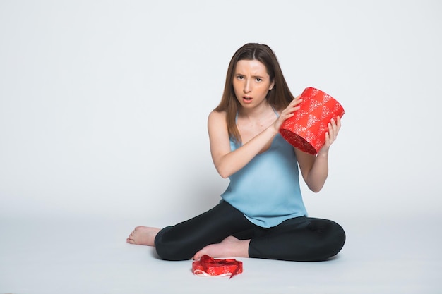 Retrato de una mujer triste de pie con una caja de regalo abierta aislada en un blanco