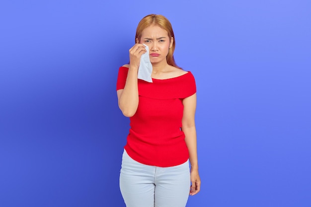 Retrato de una mujer triste que está llorando limpiándose las lágrimas de los ojos con tejido aislado en un fondo morado