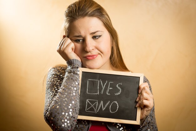 Retrato de mujer triste sosteniendo pizarra con respuesta negativa marcada