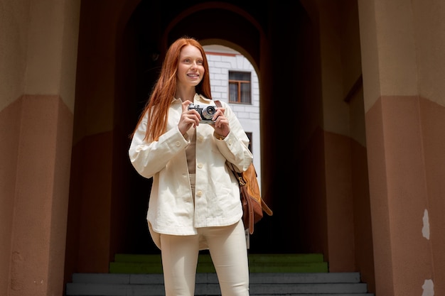 Retrato de mujer turista pelirroja tomando fotos de arquitectura en cámara de película retro