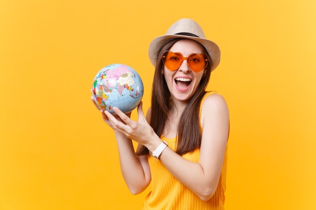 Retrato de mujer turista con sombrero de verano, gafas naranjas en manos globo aislado sobre fondo amarillo. Viajar al extranjero para viajar los fines de semana de escapada. Concepto de viaje de vuelo aéreo. Detenga la basura de la naturaleza.