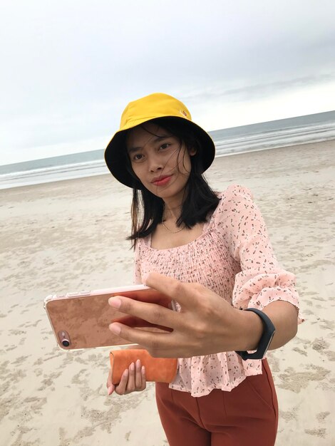 Foto retrato de una mujer usando un teléfono móvil en la playa contra el cielo