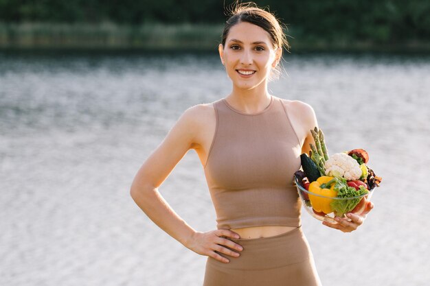 Retrato de una mujer vegana feliz sosteniendo un plato de verduras frescas al aire libre