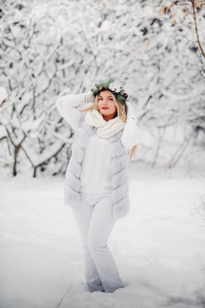 Retrato de una mujer vestida de blanco en un bosque de invierno. Chica con una corona en la cabeza en un bosque de invierno cubierto de nieve.