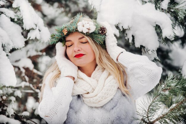 Retrato de una mujer vestida de blanco en un bosque de invierno. Chica con una corona en la cabeza en un bosque de invierno cubierto de nieve