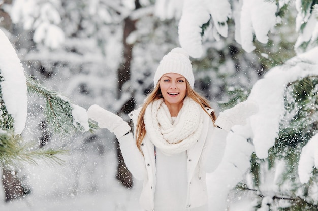 Retrato de una mujer vestida de blanco en un bosque de invierno. Una niña con un sombrero blanco en la cabeza en un bosque de invierno cubierto de nieve