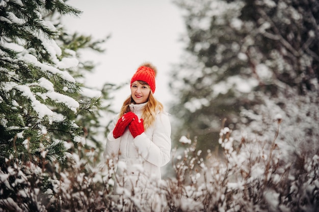 Retrato de una mujer vestida de blanco y un sombrero rojo en un bosque de invierno. Chica en un bosque de invierno cubierto de nieve