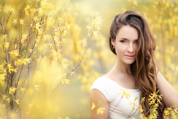 Retrato de una mujer con un vestido blanco sobre un fondo de arbustos amarillos con flores.