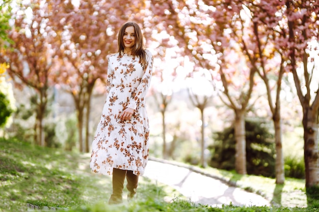 El retrato de la mujer en un vestido bonito con las flores disfruta del jardín verde floreciente en día de primavera. Concepto de moda y estilo.