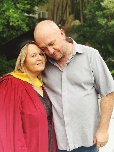 Foto retrato de una mujer con vestido de graduación mientras está de pie con un hombre en el campo