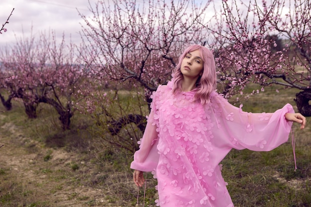 Retrato de mujer con un vestido rosa con flores se encuentra junto a un melocotonero