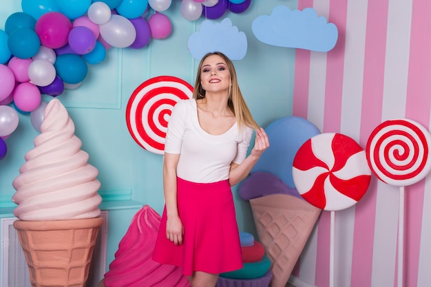 Retrato de mujer en vestido rosa sobre fondo decorado con enormes caramelos y helados