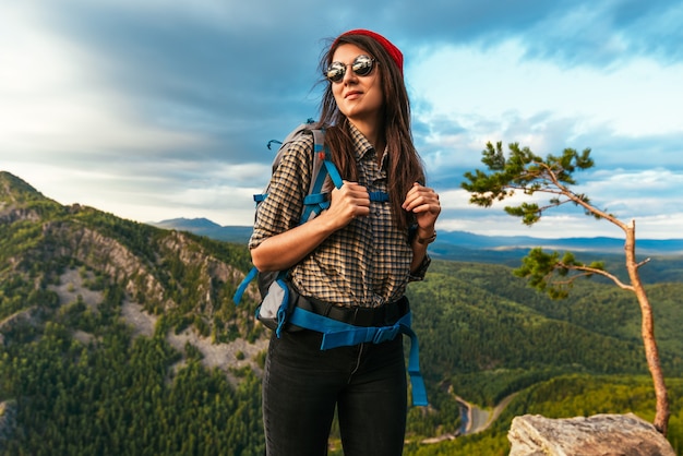 Retrato de una mujer viajera en las montañas. Concepto de aventura, viajes y senderismo. Una mujer feliz con una gorra roja disfrutando de la luz del sol durante una caminata en las montañas. Turista con gafas