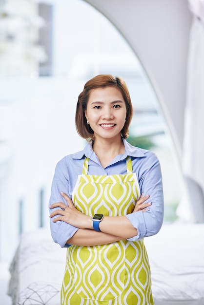 Retrato de mujer vietnamita joven feliz en delantal sonriendo, brazos cruzados