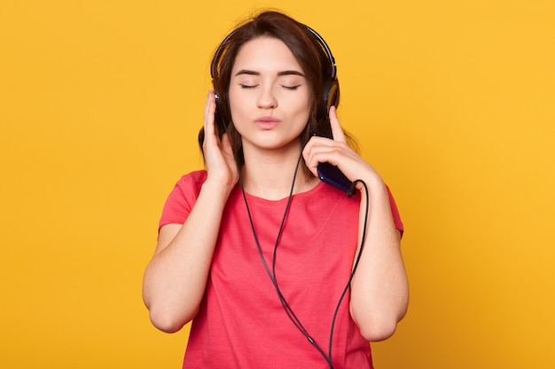 Retrato de mujer viste camiseta roja, joven mujer escuchando música a través de auriculares