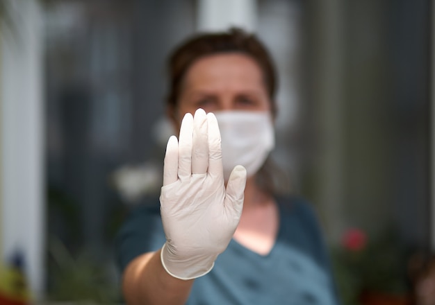 Retrato de mujeres asustadas que muestran la señal de no, cruzando los brazos, manteniendo la distancia, usando guantes y máscara antibacteriana, mirando directamente a la cámara, en cuarentena.