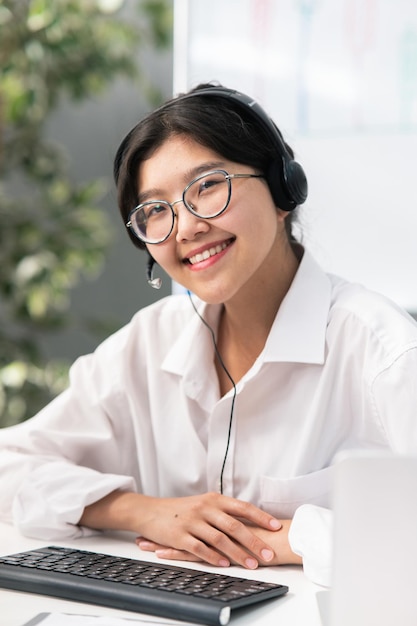 Retrato de mujeres elegantes con gafas con belleza asiática coreana se sienta en la oficina de la empresa con auriculares