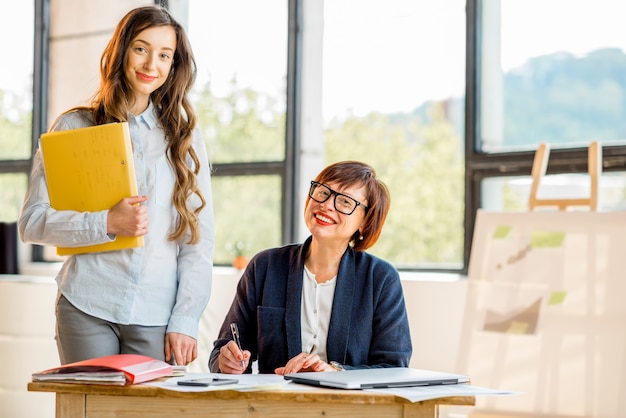 Retrato de mujeres empresarias jóvenes y mayores trabajando juntos en documentos en el interior de la oficina moderna