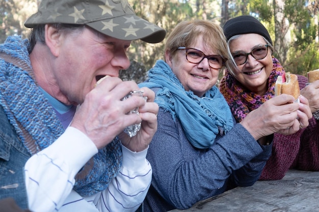 Retrato de mujeres mayores sonrientes comiendo con un amigo en el bosque