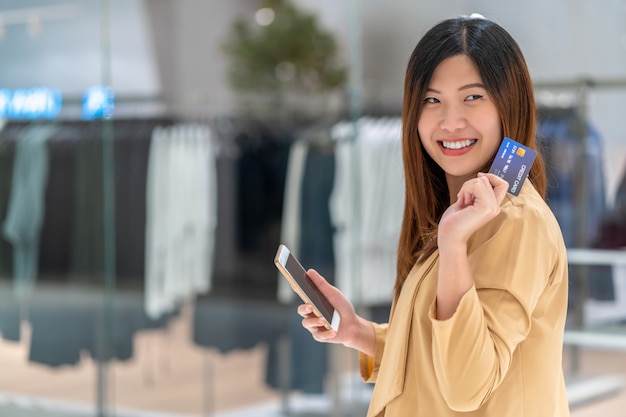 Retrato mulher asiática usando cartão de crédito com telefone móvel esperto para compras on-line na loja de departamentos