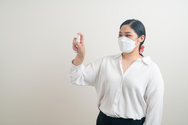 retrato mulher asiática usando máscara e usando spray de álcool com fundo branco