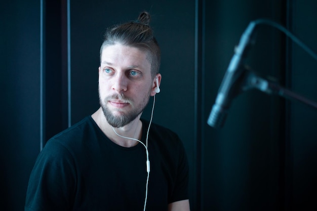 Retrato de un músico barbudo caucásico con auriculares en un estudio de grabación negro con micrófono