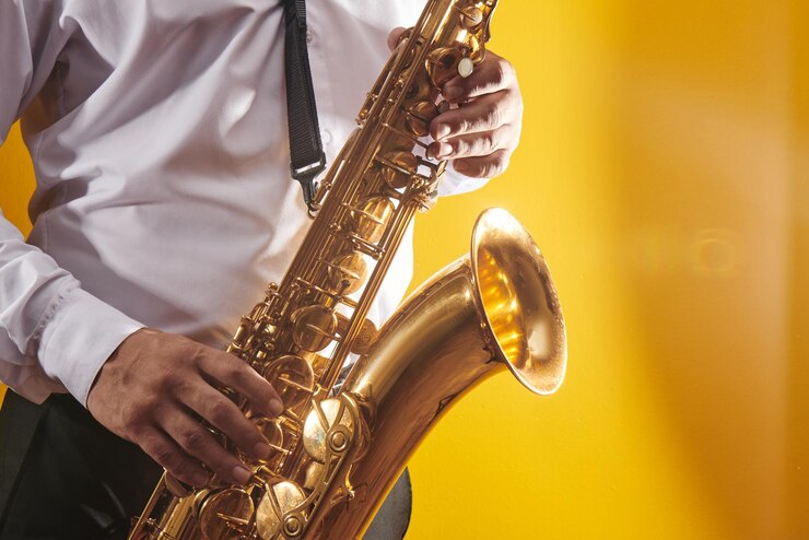 Foto retrato de músico profesional saxofonista con camisa blanca toca música de jazz en saxofón, fondo amarillo en un estudio fotográfico, vista lateral