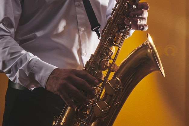 Retrato de músico profesional saxofonista con camisa blanca toca música de jazz en saxofón, fondo amarillo en un estudio fotográfico, vista lateral