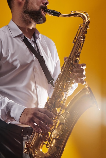 Retrato de músico profesional saxofonista con camisa blanca toca música de jazz en saxofón, fondo amarillo en un estudio fotográfico, vista lateral