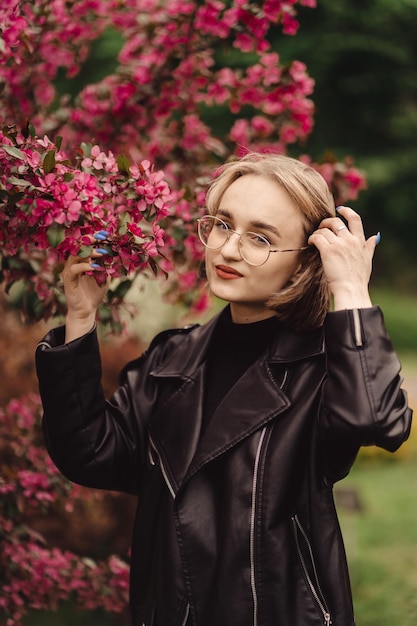 Retrato natural de una joven rubia feliz de negro en el fondo del árbol de flores rojas en otoño