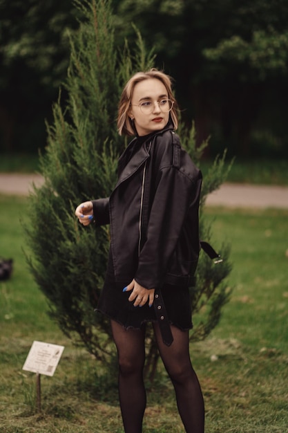 Retrato natural de una joven rubia feliz de negro en el fondo de un pequeño árbol verde en otoño