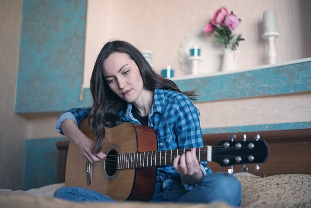 Retrato natural de una mujer dedicada a enseñar guitarra acústica en la cama en el dormitorio