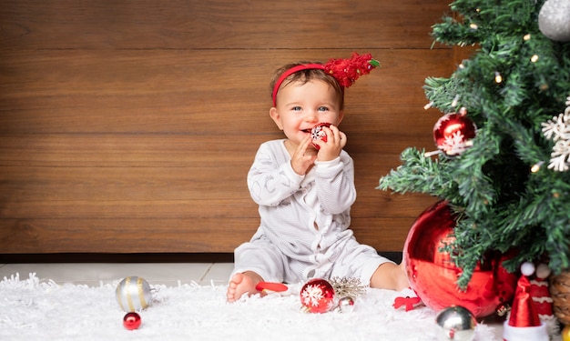 Retrato de Navidad del bebé en la pared de madera cerca del árbol de Navidad. Niño con adorno de navidad