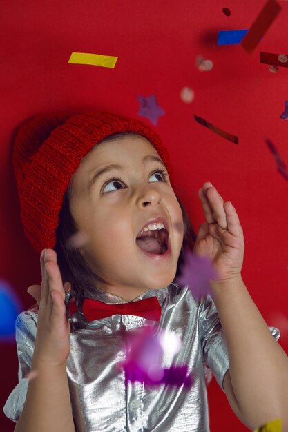 Foto retrato navideño de un niño con camisa plateada y corbata roja atrapa confeti brillante en las vacaciones