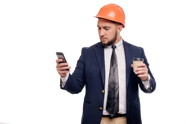 Retrato de negocios de contratista y desarrollador sorprendido, hablando de teléfono. Hombre de negocios en casco con taza de café sobre fondo blanco. Concepto de freno de café y noticias