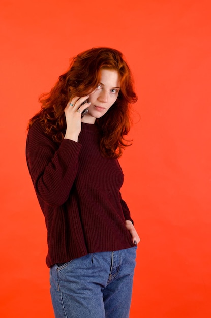 Retrato de negocios de una hermosa joven. pelo rojo rizado y ojos azules. fondo rojo Teléfono