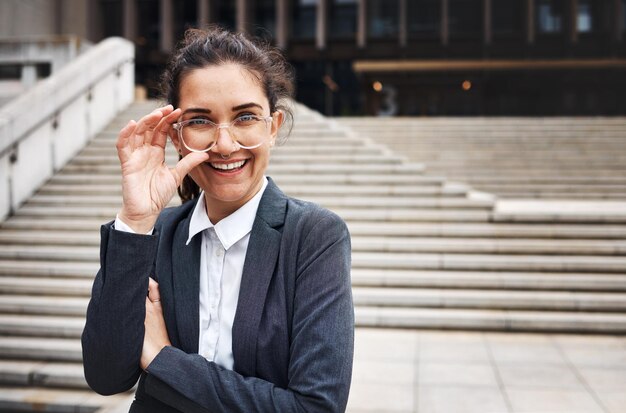 Retrato de negocios y mujeres en una ciudad, anteojos y felicidad con éxito en viajes o cara corporativa, persona femenina o abogada, anteojos al aire libre o sonrisa con visión clara, empoderamiento o profesional.