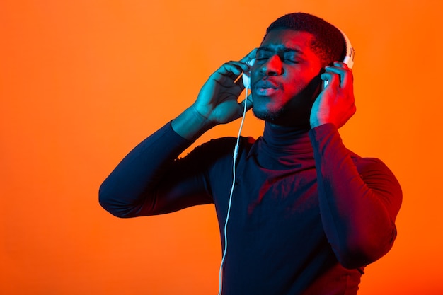 Retrato de neón de joven africano escuchando música con auriculares.