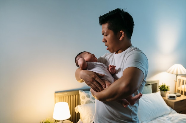 retrato nervioso asiático papá por primera vez está consolando a su enojado bebé llorando en brazos a medianoche en un dormitorio con paredes blancas en casa.