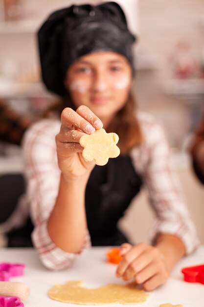 Retrato de nieto vistiendo delantal mirando a la cámara mientras sostiene la masa para galletas