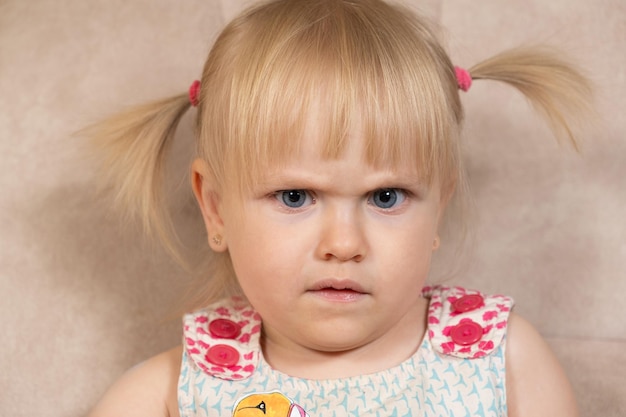 Retrato de una niña de 2 años frunciendo el ceño sospechosamente mirando a la cámara