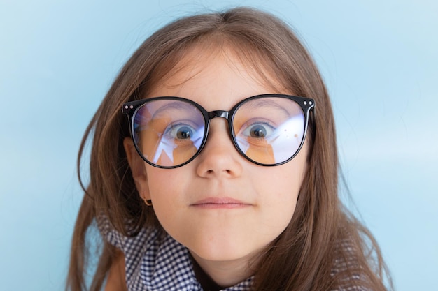Retrato de una niña de 7 años con cabello largo en anteojos con ojos saltones mira a la cámara