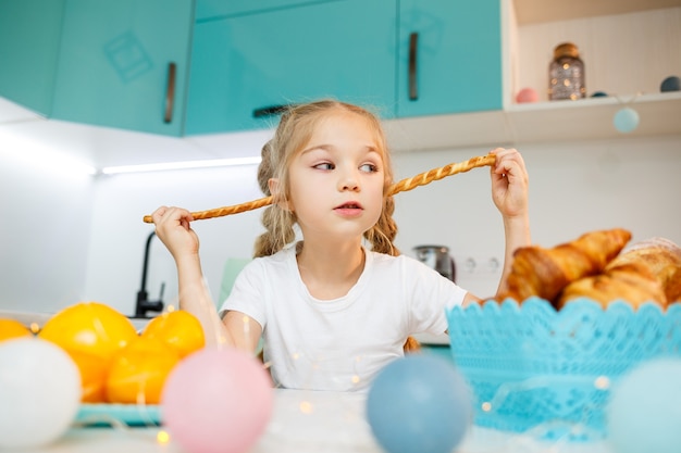 Retrato de una niña de 7 años sentada en la cocina y juega con palitos de pan. Niño desayuna en la cocina