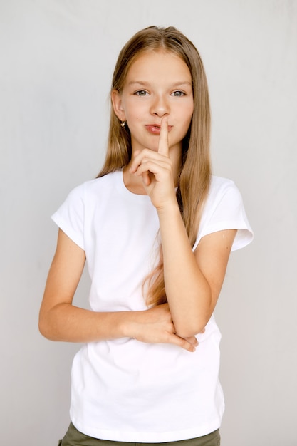 Retrato de niña adolescente sosteniendo el dedo cerca de los labios y mostrando el signo de guardar silencio