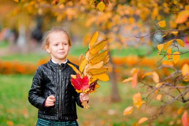 Retrato de niña adorable con ramo de hojas amarillas en otoño en scooter